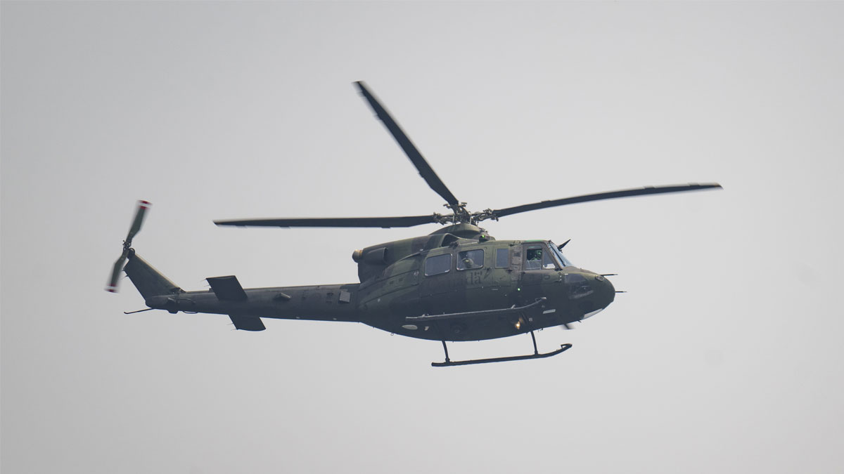 Military helicopter flying against a gray sky.