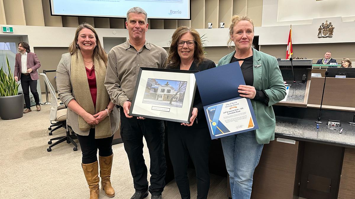 Councillor Kungl, Jeff Reid, Leanne Reid and Councillor Courser pose with a framed photo of the property and the award