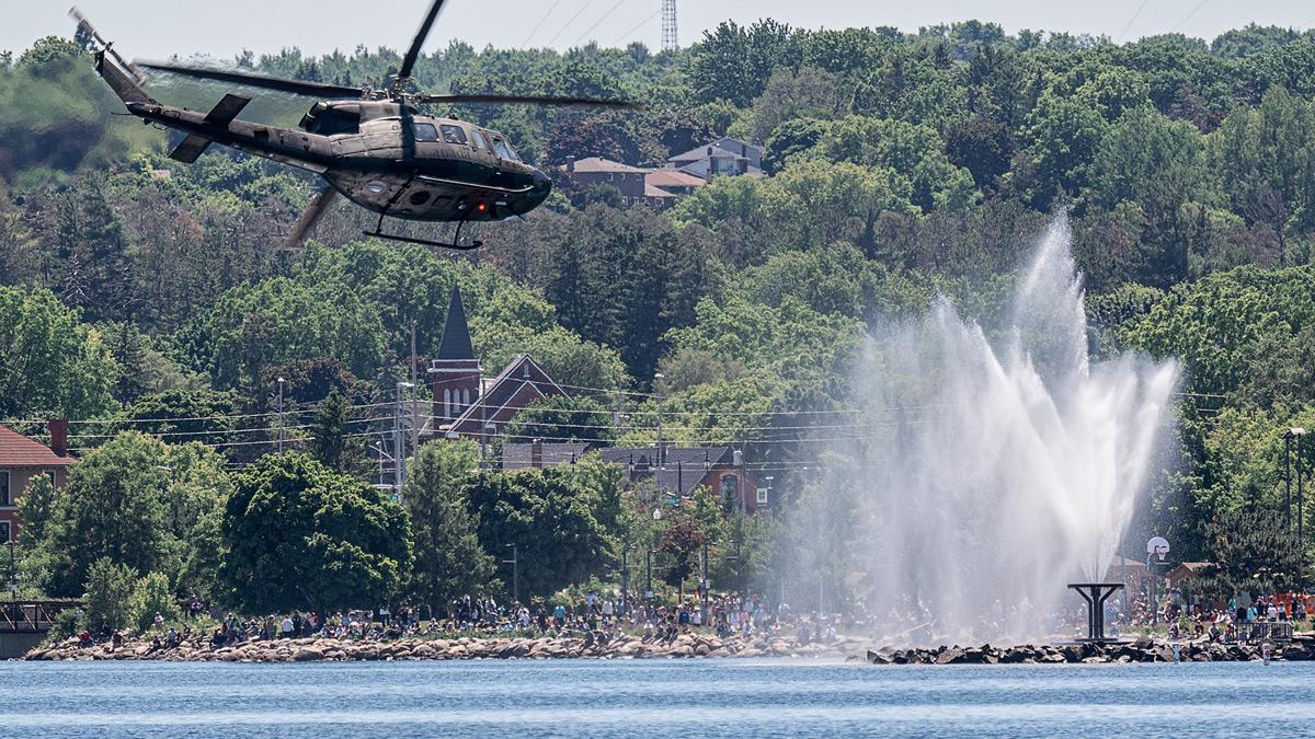 Helicopter flying over Kempenfelt Bay in front of a large crowd and water feature