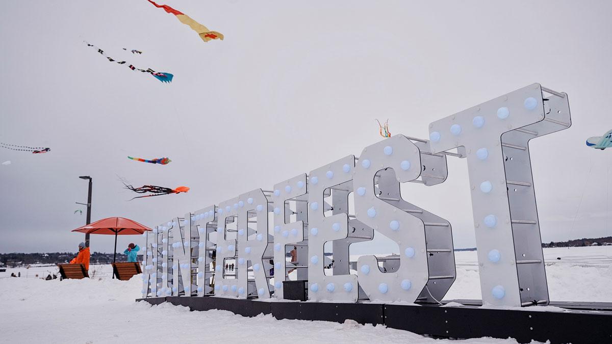 Winterfest sign with kites in the sky behind it.