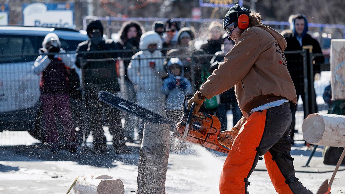 Lumberjacks sawing wood as the crowd watches.