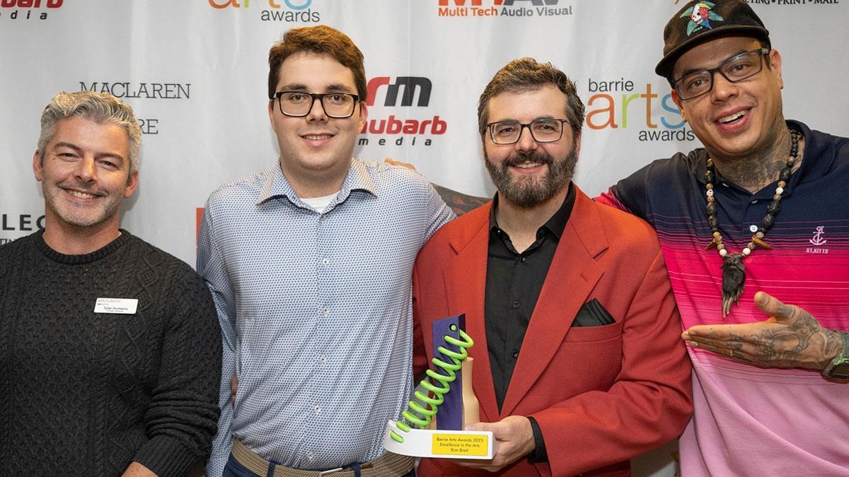 Four people stand together, smiling and holding an award, against a decorated backdrop.