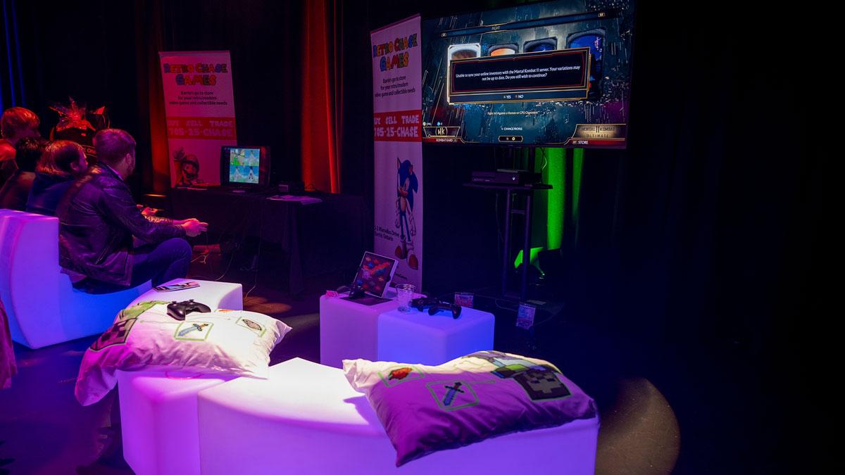 A gaming setup with a TV, controllers, and colourful seating in a dimly lit room.