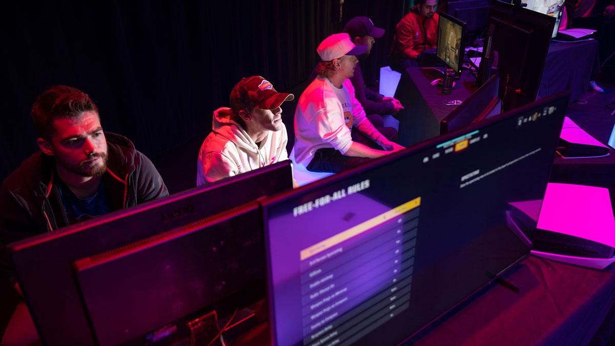 Esports competitors focus intently on screens in a dimly lit gaming venue.