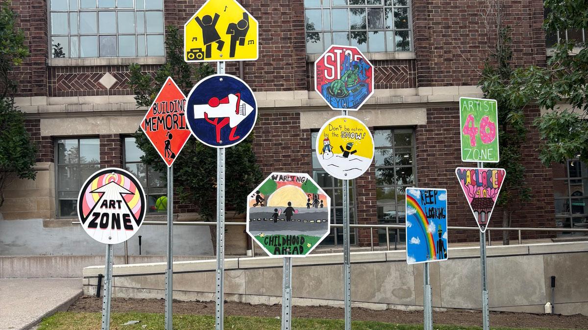A variety of colourful traffic signs displayed on poles outside a brick building.