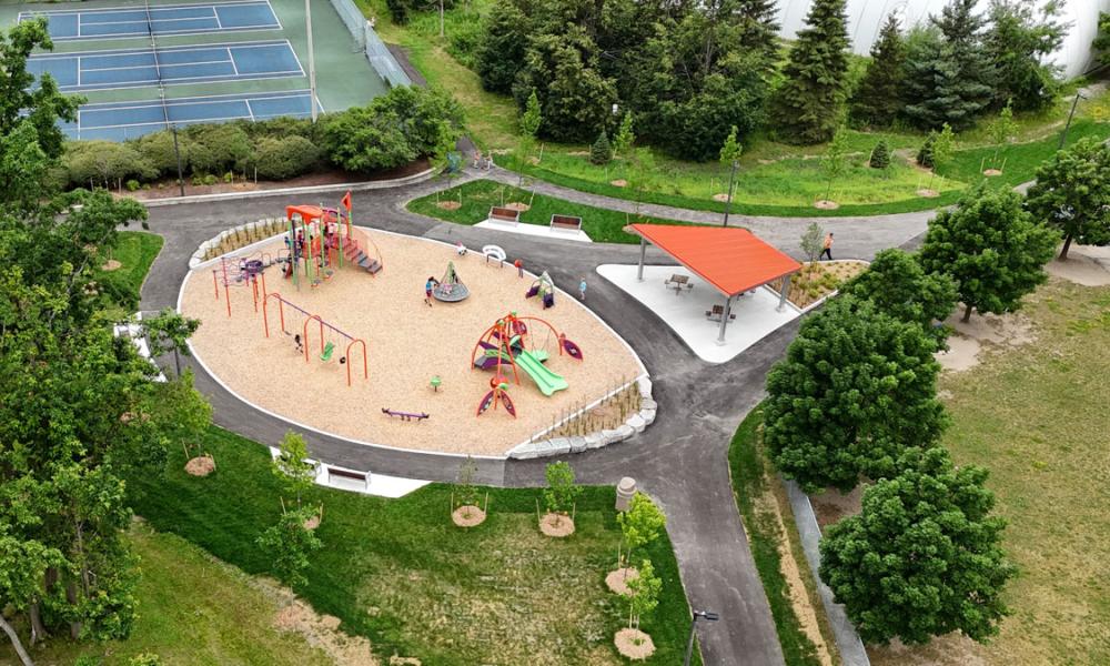 Aerial view of a playground with kids playing, surrounded by trees, and pickleball courts in the background
